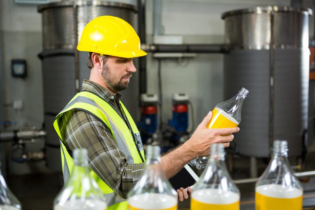 Side view of serious male worker inspecting bottles in juice factory